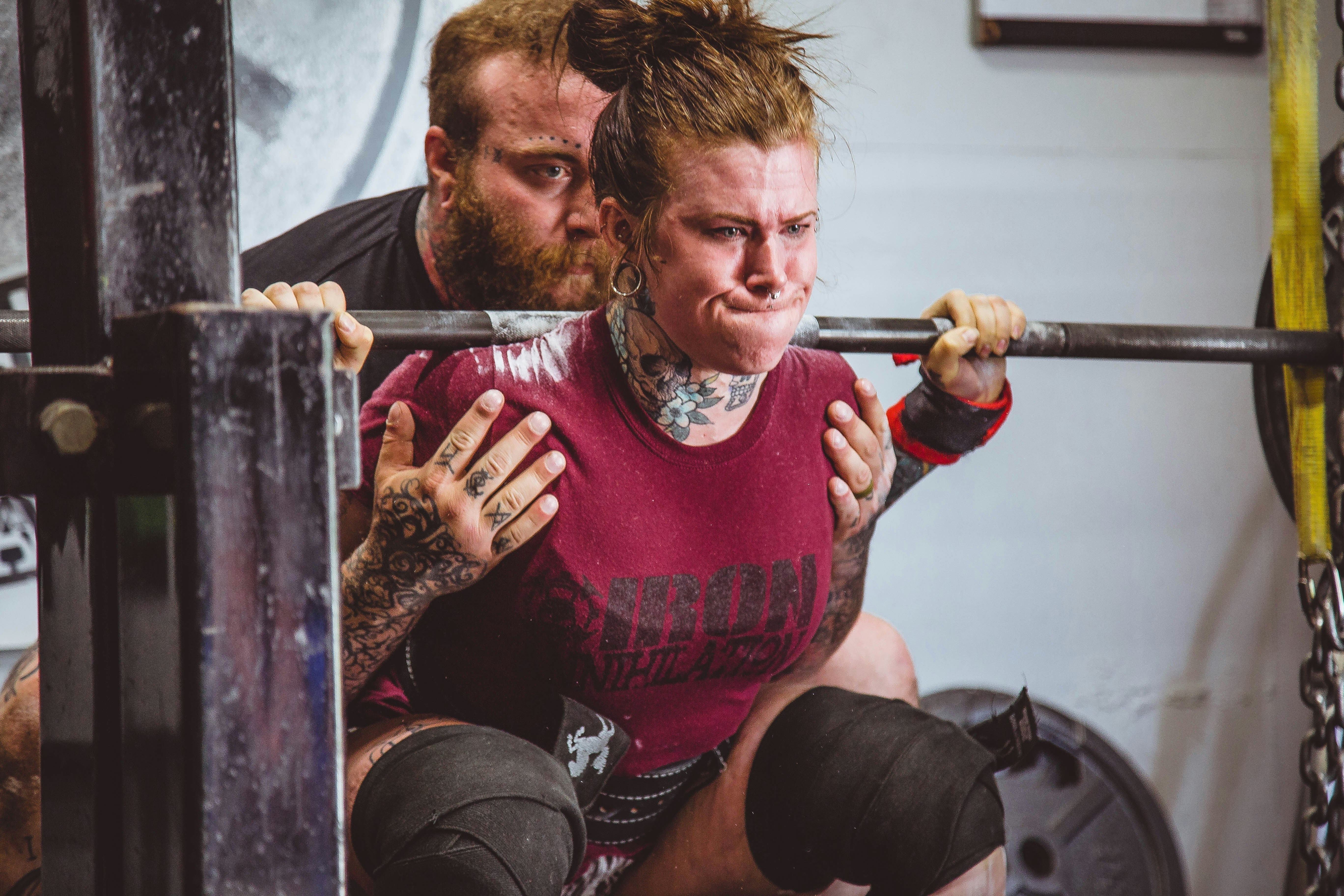Female strength athlete performing a heavy barbell squat with a spotter, representing hydration, power, performance and recovery in strength training.