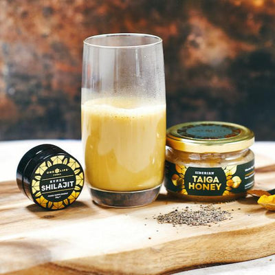 Glass of turmeric milk with honey and shilajit on wooden surface